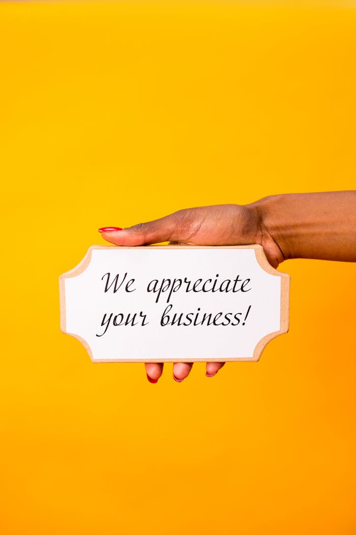 A hand holding a sign with 'We appreciate your business!' against a yellow background.